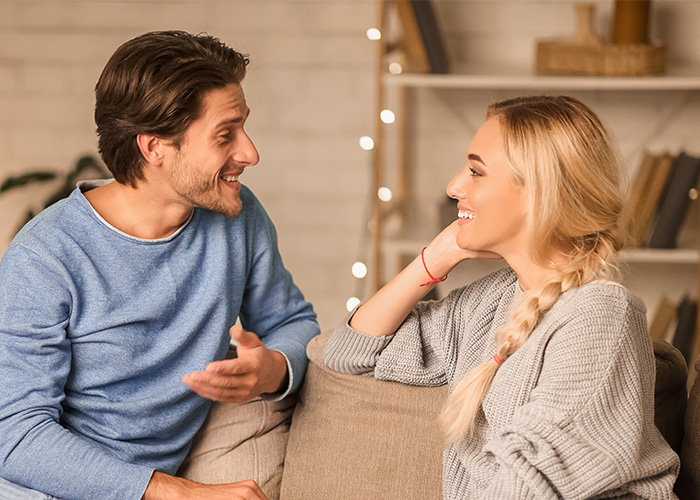 Young rich couple smiling and talking on a cozy couch, reflecting moments when wealth shapes different normal lives. - 9