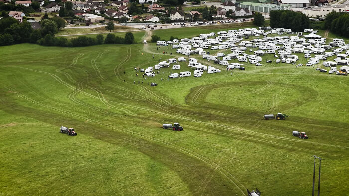 Aerial view of a farmer spraying manure on a large field near squatters' caravans during removal.