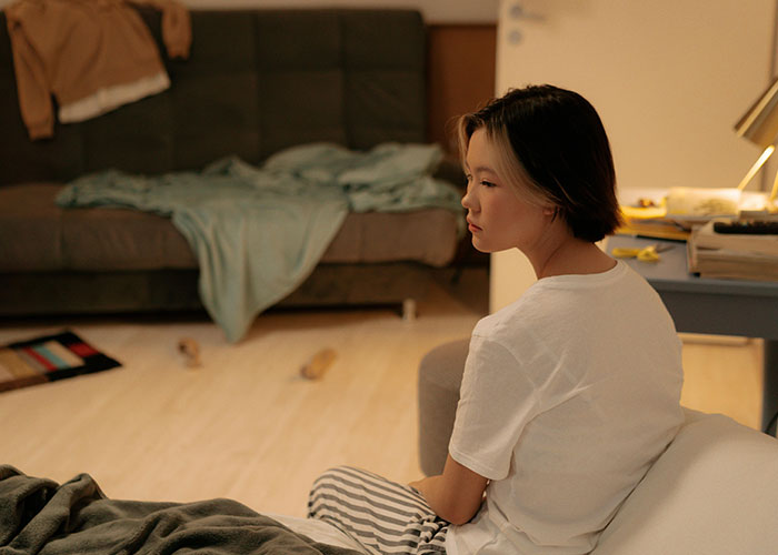 Young woman looking thoughtful and alone in a dimly lit room, reflecting on wild and embarrassing drinking stories.