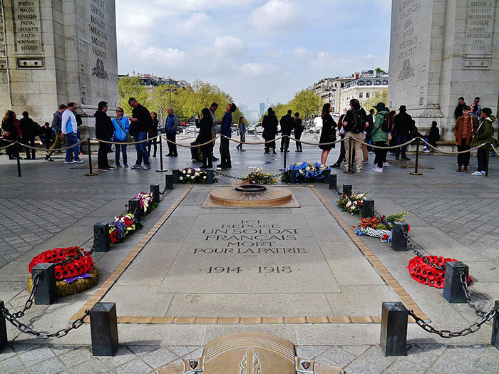 Tomb of Unknown Soldier surrounded by flowers and visitors, related to man arrested for lighting cigarette on memorial.