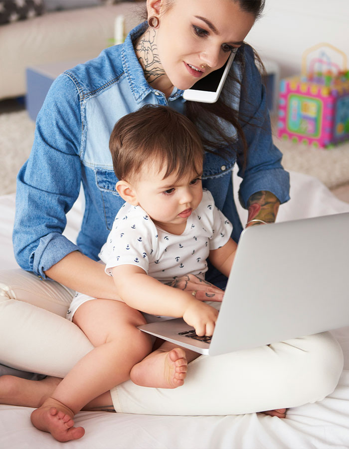 Working mom in the U.S. multitasking with child on laptop and phone, illustrating challenges of being a working mother. Working mom in the U.S. multitasking with child on laptop and phone, illustrating challenges of being a working mother.