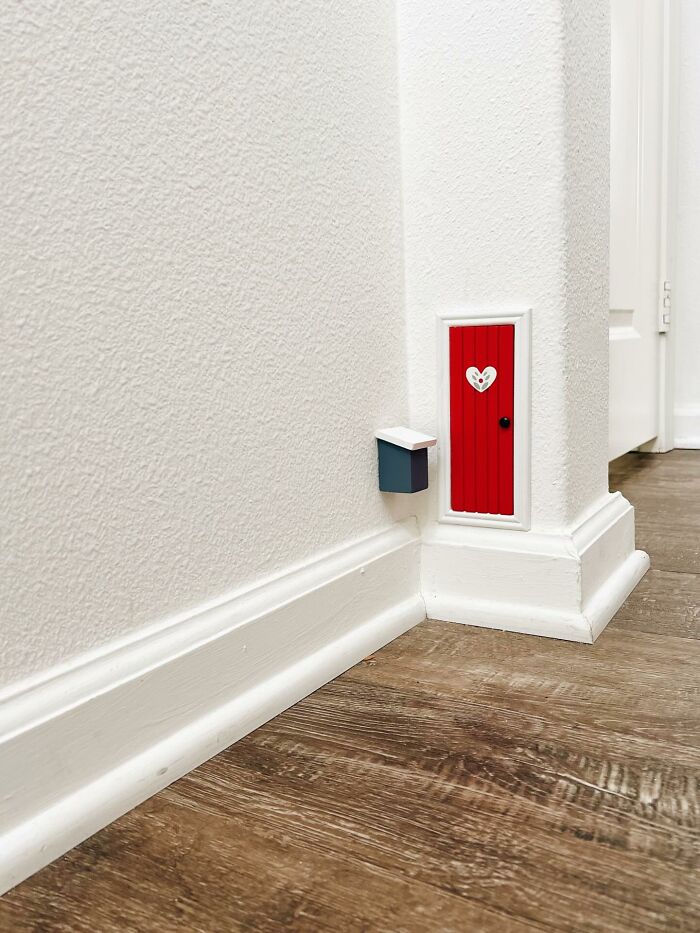 Small decorative red fairy door with a heart on a white wall, adding magical decor pieces to a cozy home corner.