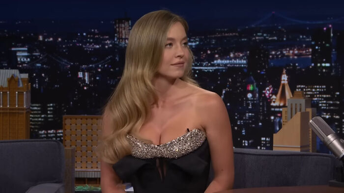 Female celebrity in a sparkling black dress during a late-night talk show, representing Hollywood leading A-listers.