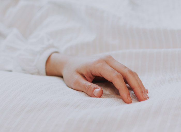 Hand of a person resting on a white bed sheet, representing professionals who work in other people’s homes.