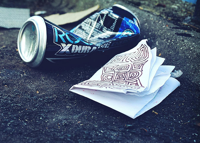 Crushed soda can and folded paper with doodles on asphalt, illustrating careless behavior like driving over the speed limit.