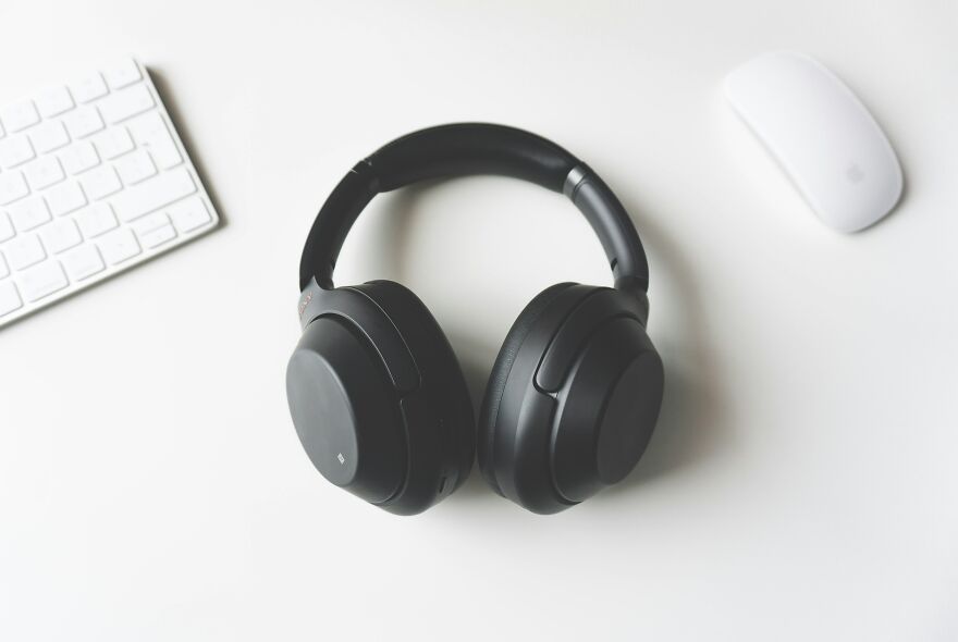 Black over-ear headphones placed on a white desk with a keyboard and mouse, related to neurologist warnings on post-exercise habits.
