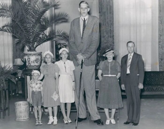 Vintage black and white photo of an unusually tall man standing with a group, unsettling images from morbid knowledge.