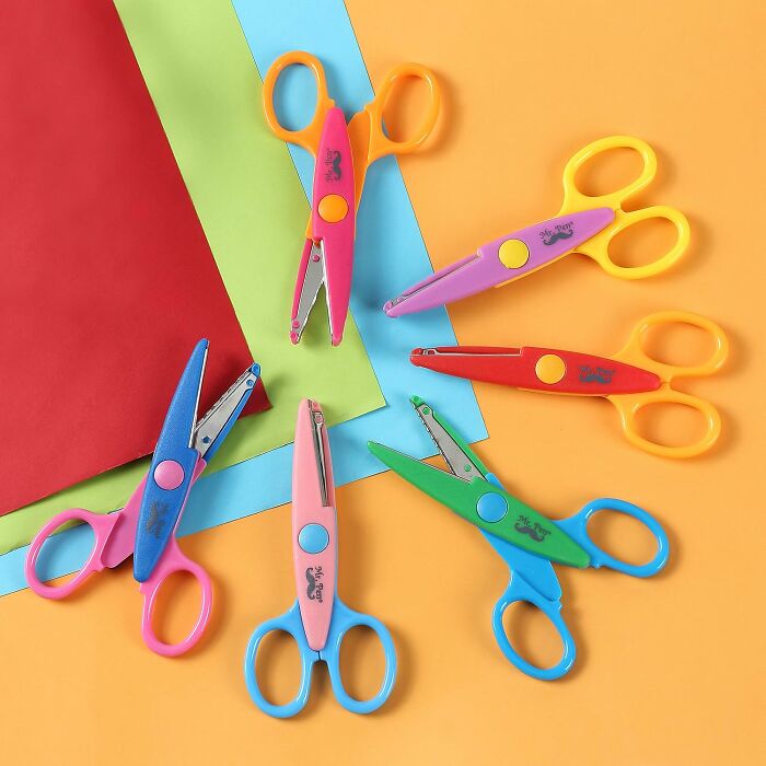 Colorful back to school scissors arranged in a circle on a yellow surface with multicolored craft paper sheets.