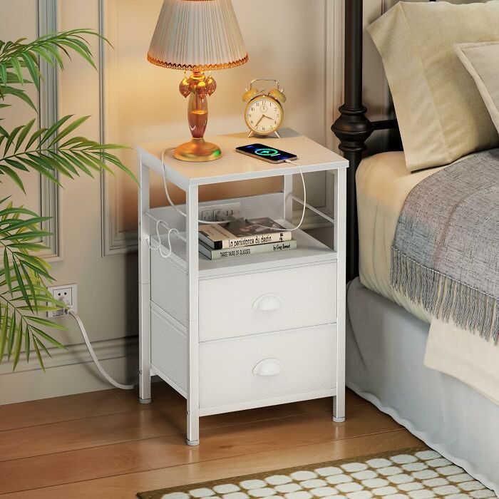 White compact bedside table with drawers, a lamp, alarm clock, and phone charging, ideal for tiny apartment furniture.