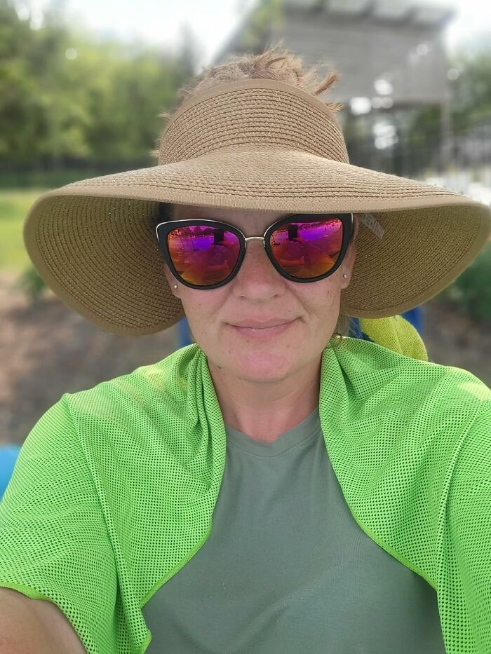 Woman wearing a wide sun hat and sunglasses outdoors using heatwave hacks to stay cool during summer heatwave conditions.