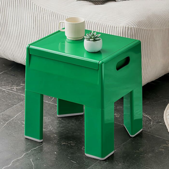 Green tiny apartment furniture side table with a white mug and small potted succulent on top beside a beige sofa.