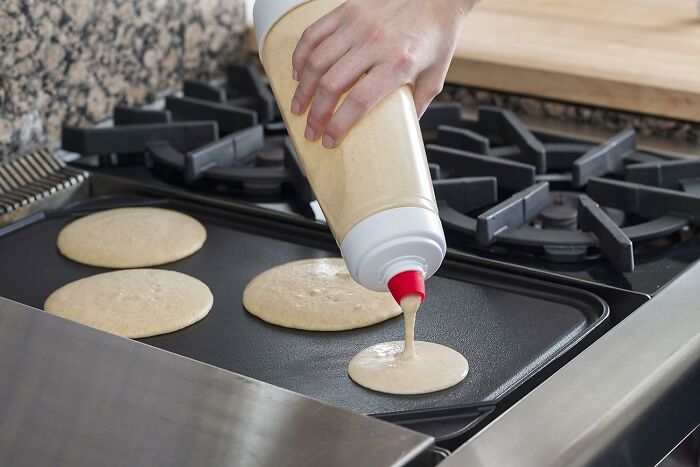 Hand pouring batter from a squeeze bottle onto a griddle, demonstrating smart kitchen tools in use.