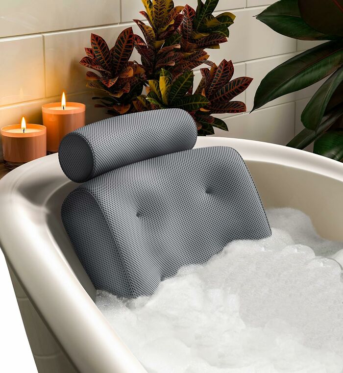 Gray bath pillow in a bubble-filled tub with lit candles and decorative plants, a top trending add to cart find on Amazon.