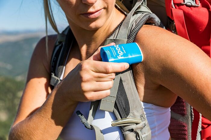 Woman applying sunscreen while hiking outdoors, demonstrating heatwave hacks for staying cool during summer heat.