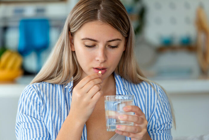 Young woman taking a pill with water, illustrating aspects of modern life close to breaking down according to netizens.