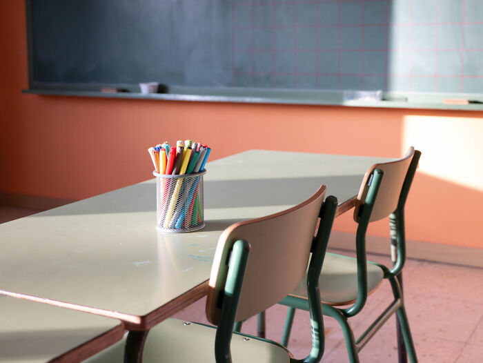 Classroom table and chairs with colored pencils in a holder, setting the scene for school kids' wildest confident moments.