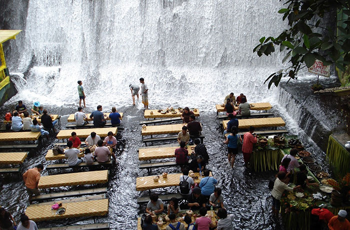 Creative bars and restaurants with dining tables in shallow water near a large waterfall attracting many visitors worldwide