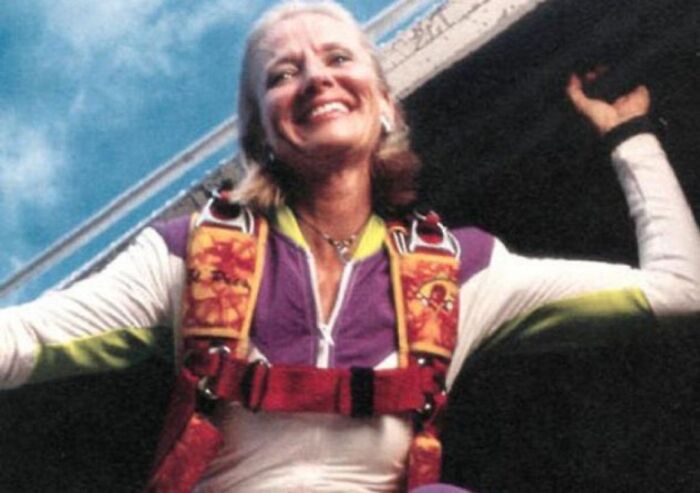 Woman smiling and wearing colorful parachute gear preparing for a skydive in an unsettling morbid knowledge image.