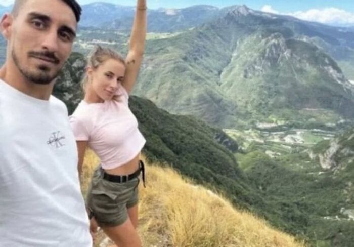 Couple posing for a selfie on a mountain trail with vast landscape views, fitting morbid knowledge unsettling images theme.