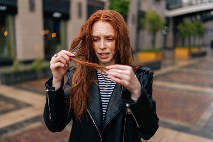 Young woman outdoors looking stressed while holding her hair, illustrating challenges related to shopping addictions.