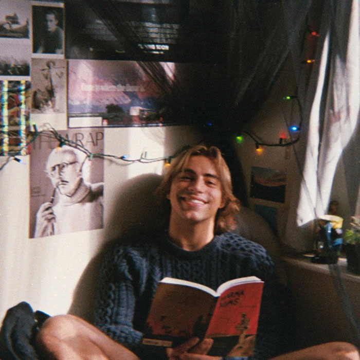 Young man reading a book in a cozy room decorated with posters and string lights, reflecting on Chase Filandro.