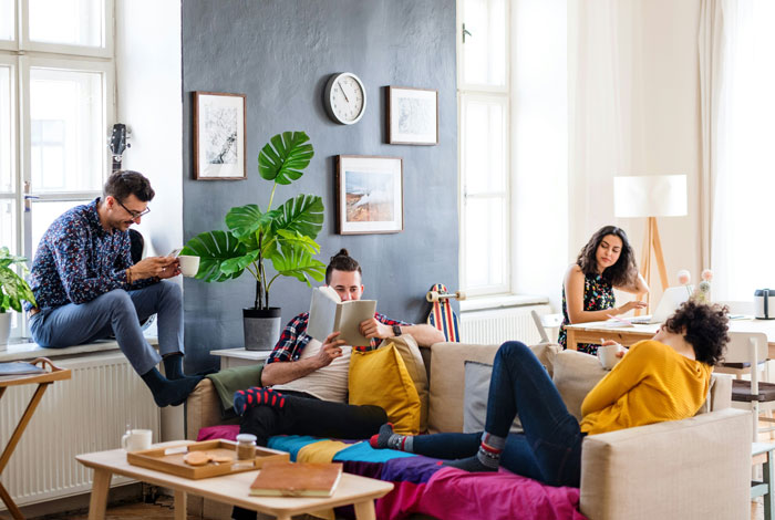 Group of roommates relaxing and engaging in activities in a bright living room with no AC visible.