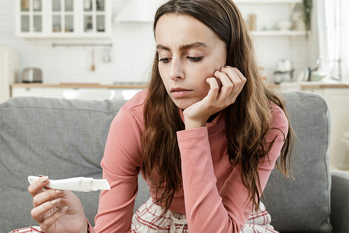 Teen girl sitting on a couch looking at a pregnancy test, showing concern about keeping her baby and lack of support.