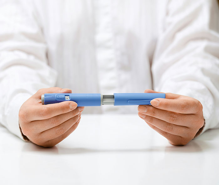 Hands holding a blue medical injector pen related to Ozempic vulva side effects from weight-loss medication use.