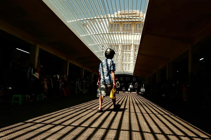 Person wearing a helmet walking through a sunlit market corridor, showcasing candid everyday moments from Asia.