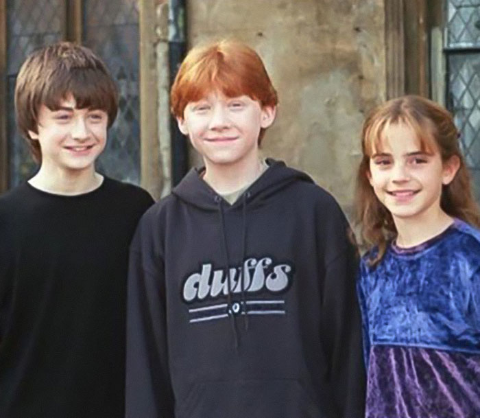 Three young actors smiling together on set, not related to Emma Watson wearing a see-through dress on a hike.