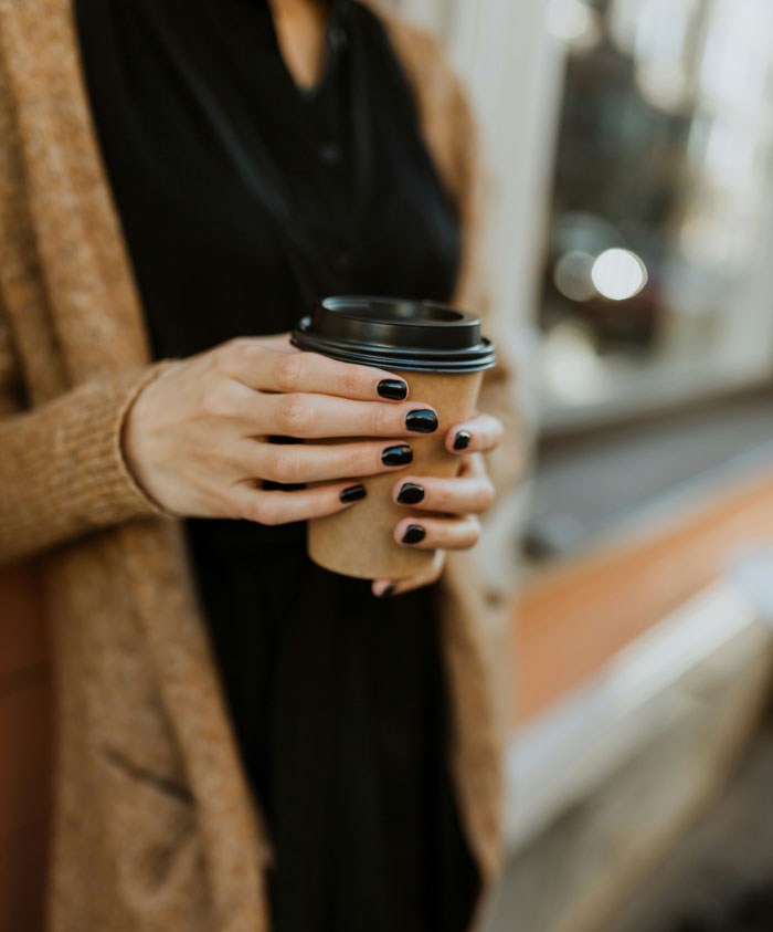 Person with black nail polish holding a to-go coffee cup, illustrating things Americans do that make them stand out abroad.