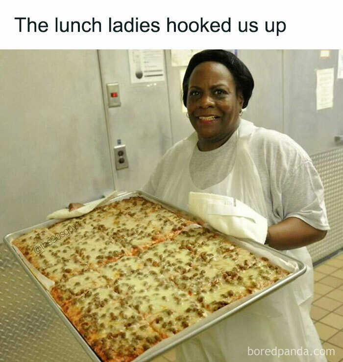 Lunch lady holding a large tray of pizza, evoking ‘90s nostalgia and good old times memories from school lunches.