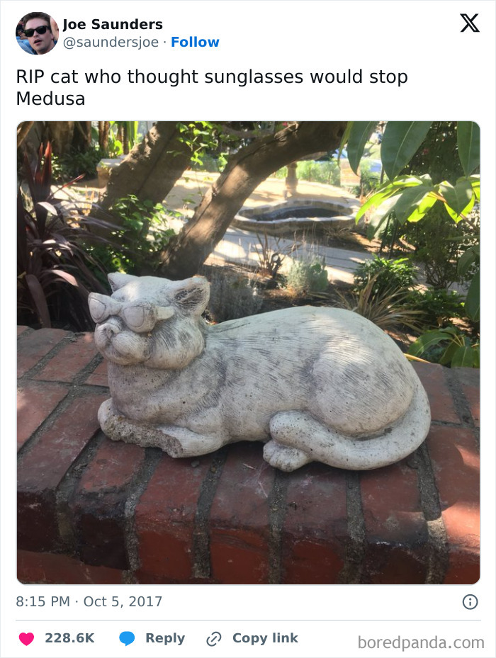 Stone cat statue wearing sunglasses on a brick wall, humorously referencing mythology and chaotic memes about ancient reality TV.