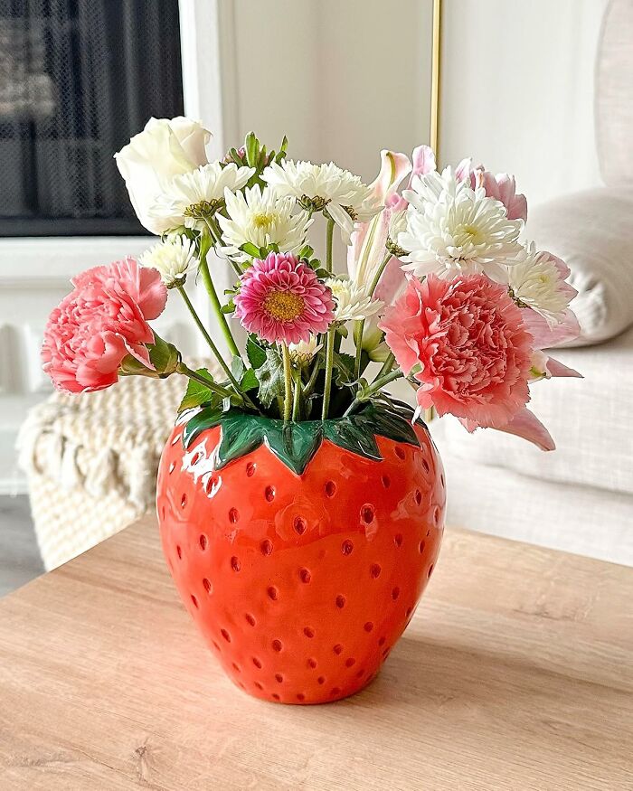 Bright strawberry-shaped vase holding a colorful bouquet of flowers, showcasing useful decor items for stylish living spaces.