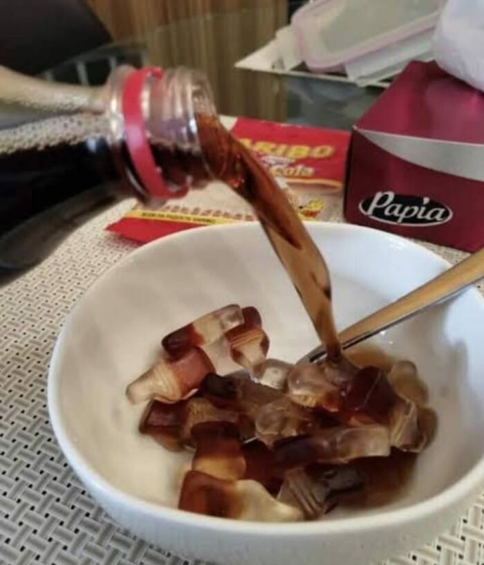 Pouring soda over cola-shaped candy pieces in a bowl, illustrating unhealthy food choices affecting physical and mental health.
