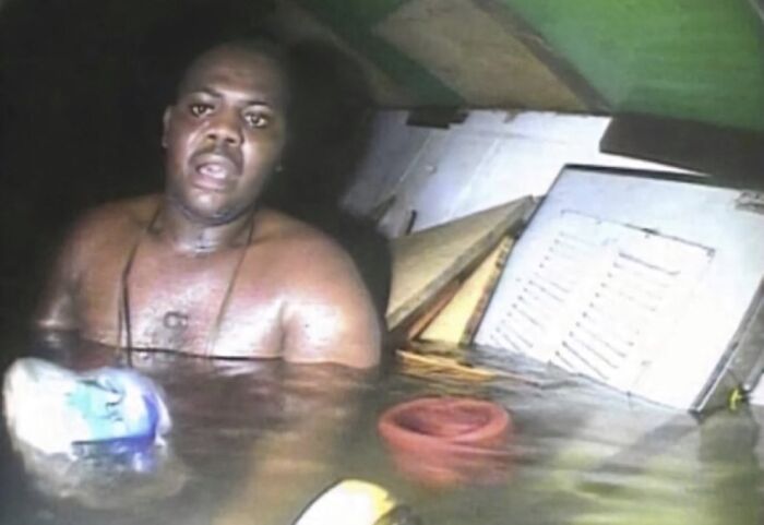 Man partially submerged in water inside a flooded area, an unsettling image related to morbid knowledge online group content.
