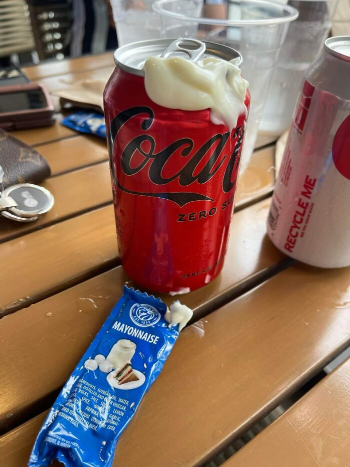 Can of soda with spilled mayonnaise on top and a torn mayonnaise packet on a wooden table, illustrating harmful food choices.