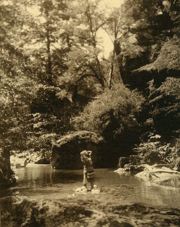 Native tribes member standing in a shallow river surrounded by forest, capturing the strength of native tribes in the 1900s.