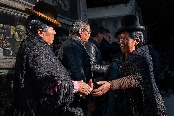 Two women wearing traditional clothing and bowler hats greeting each other, capturing the beauty of cultures in travel photography.