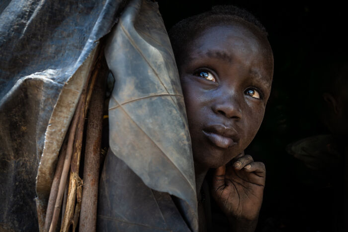 Close-up of a young person emerging from a dark shelter, showcasing cultural beauty captured by a photographer traveling over 50 countries.