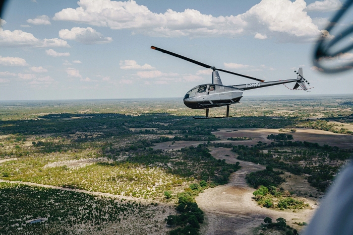 Helicopter flying over the lush Okavango Delta landscape under a partly cloudy sky during daytime.