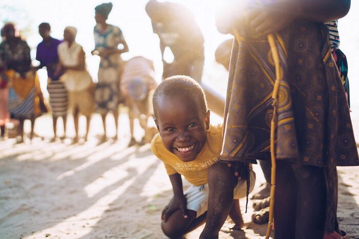 Smiling child crouching in bright sunlight with a group of people in the background in the Okavango Delta region.
