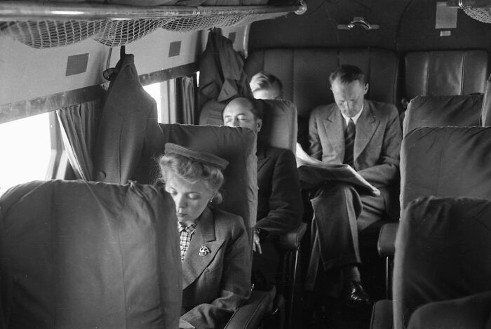Vintage black and white photo of passengers in stylish attire inside a glamorous airplane cabin from the golden age of flying.