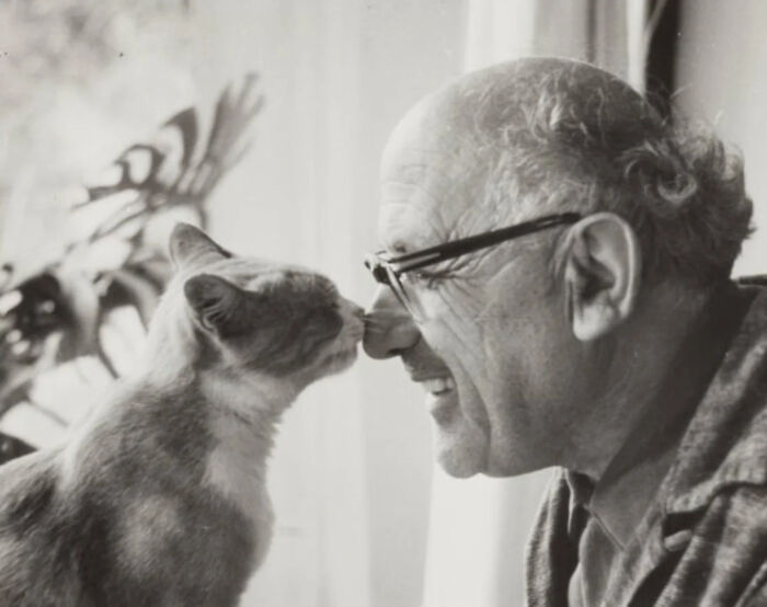Vintage cat photo showing a man with glasses and a cat touching noses in a warm, tender moment.