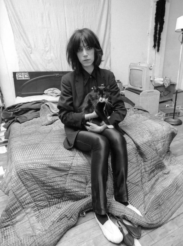 Woman sitting on bed holding a vintage cat in a black and white photo from before the internet era.