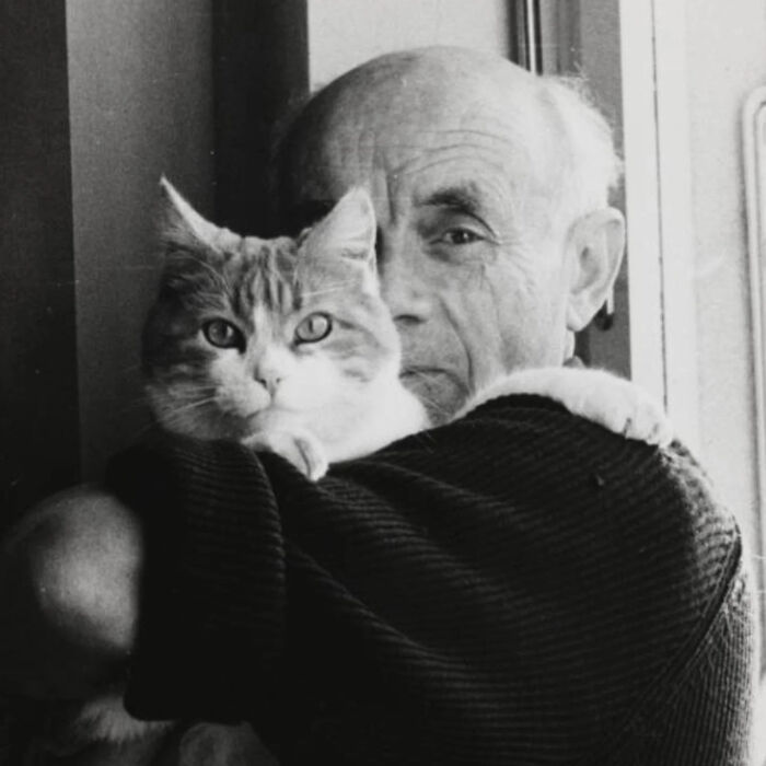 Black and white vintage cat photo showing an elderly man holding his cat close in a cozy indoor setting.