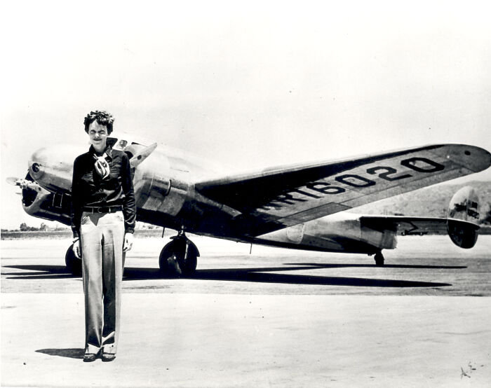 Amelia Earhart standing in front of a vintage airplane, linked to the world's most baffling unsolved mysteries.