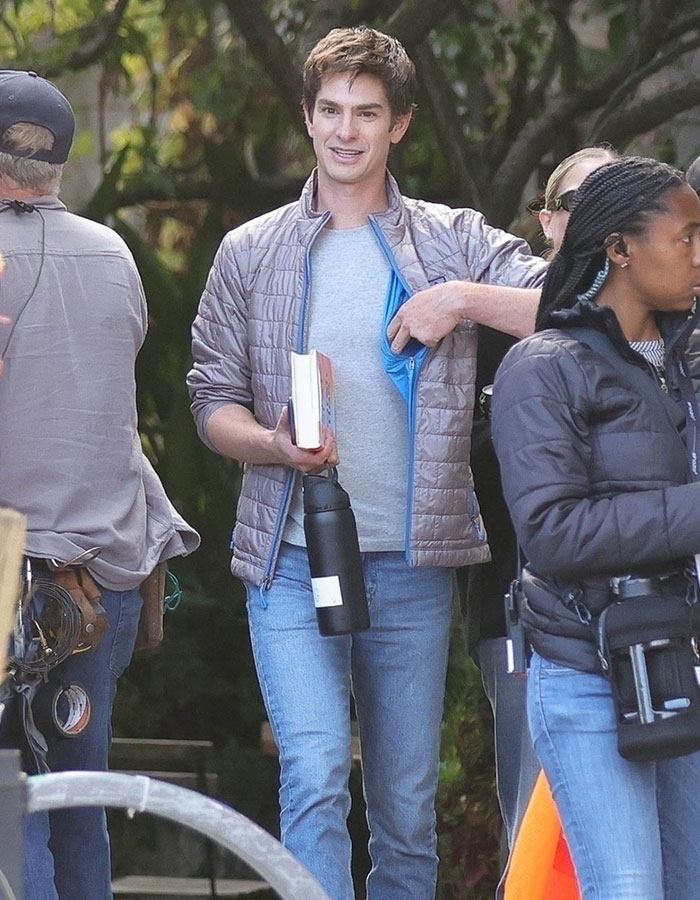 Andrew Garfield on set wearing a grey jacket holding a book and water bottle sparking botox buzz.