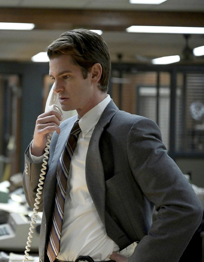 Andrew Garfield in a suit, talking on a corded phone, showcasing a look that sparks major botox buzz in a period office setting.