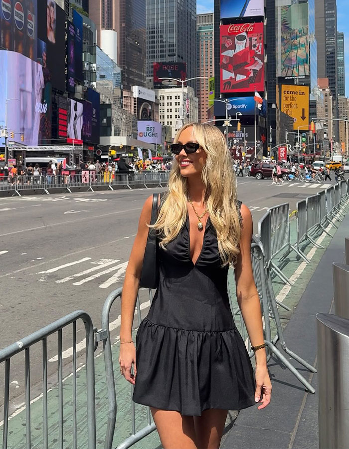 Woman who slept with 583 men in a day wearing black dress and sunglasses walking in busy city street.
